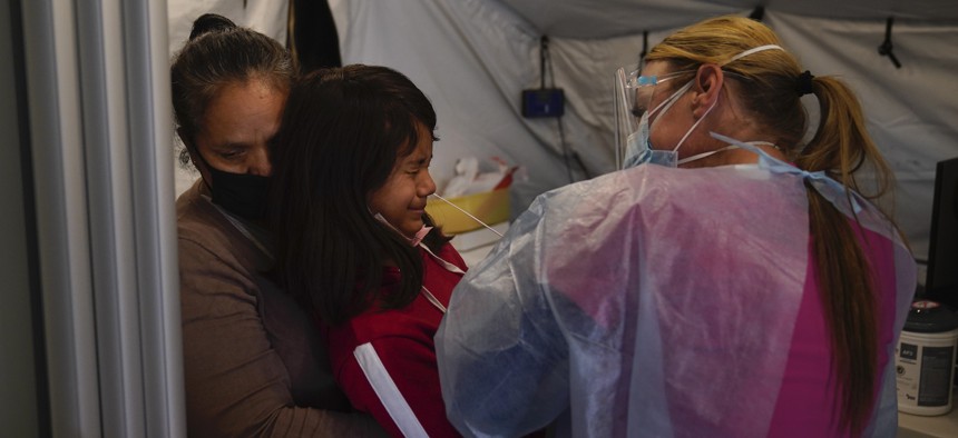 Held by grandmother Maria Ortiz, 11-year-old Star Estrada, center, grimaces as registered nurse Angela Coomds collects a nasal swab sample from her in a COVID-19 triage tent at Providence Holy Cross Medical Center in the Mission Hills section of Los Angeles, Tuesday, Dec. 22, 2020.