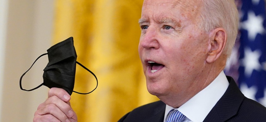 President Biden holds up a mask July 29 as he announces that millions of federal workers must show proof they've received a coronavirus vaccine or submit to regular testing and stringent social distancing, masking and travel restrictions. 