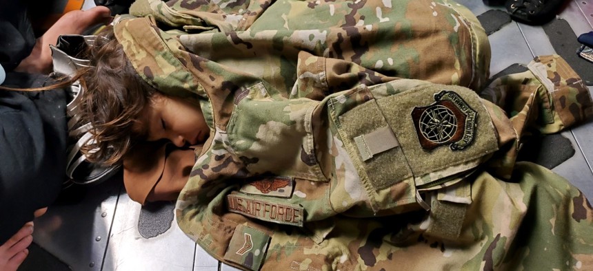 An Afghan child sleeps on the cargo floor of a U.S. Air Force C-17 Globemaster III, kept warm by the uniform of the C-17 loadmaster, during an evacuation flight from Kabul, Afghanistan, Aug. 15, 2021.