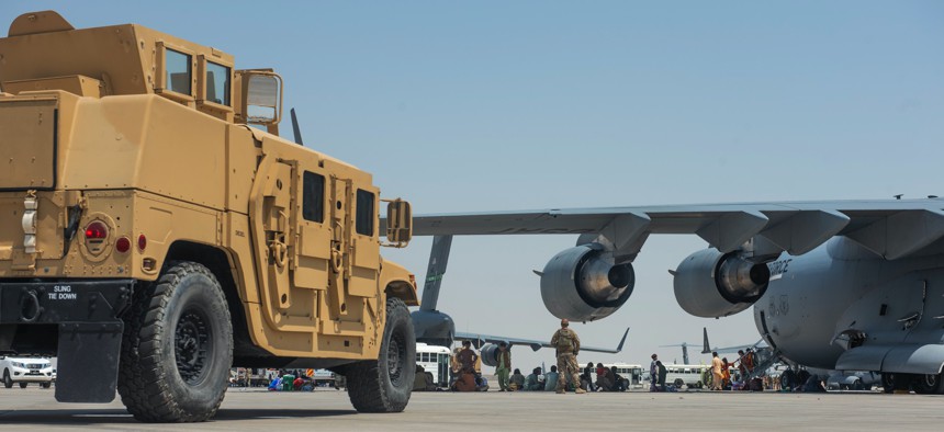 Evacuees from Kabul, Afghanistan, wait under the wing of C-17 Globemaster lll at an undisclosed location after arriving on Aug. 20, 2021.