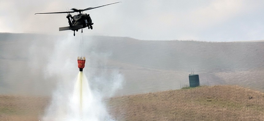 U.S. Army HH-60 Black Hawk pilots and flight crew assigned to Charlie Company, 3rd Battalion, 25th Aviation Regiment, 25th Combat Aviation Brigade, 25th Infantry Division, help local firefighters extinguish a fire using a Bambi bucket near the Pohakuloa Training Area, Hawaii, July 31, 2021.