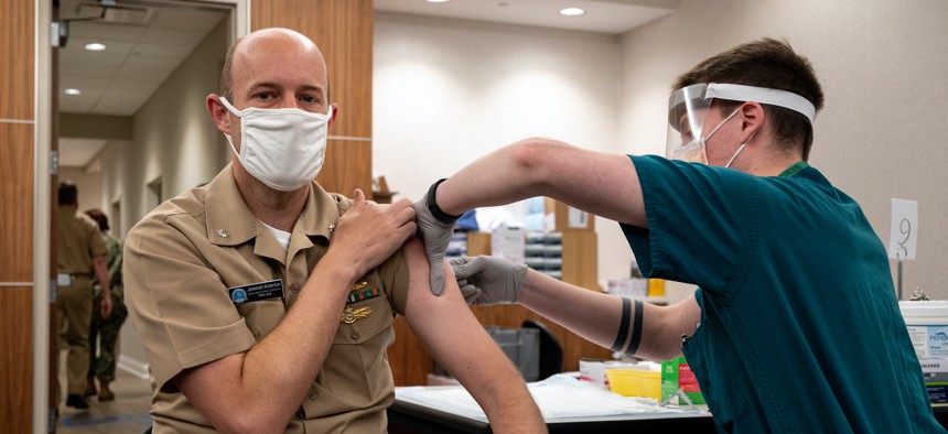 Cmdr. Jeremiah Anderson, left, receives the first COVID-19 vaccine dose administered during a vaccination event held onboard Washington Navy Yard in April 2021.