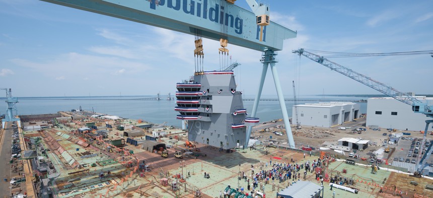 The island of the aircraft carrier USS John F. Kennedy (CVN 79) is landed onto the flight deck during a mast-stepping ceremony at Huntington Ingalls Industries Newport News Shipbuilding in Newport News, Va., May 29, 2019. 