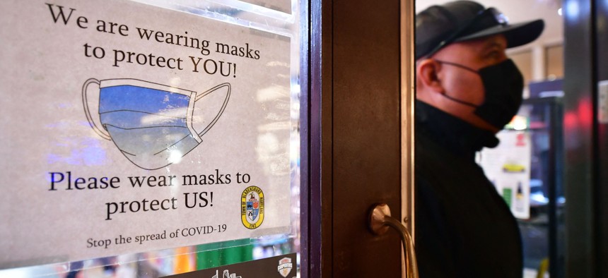 A man wears his mask as he walks past a sign posted on a storefront reminding people to wear masks in Los Angeles in February.