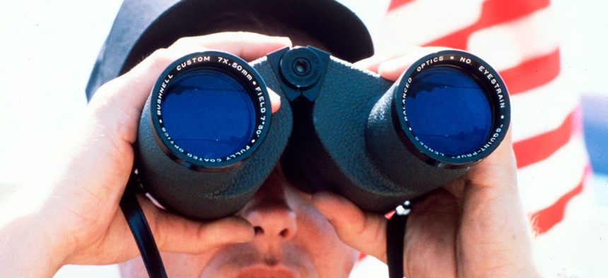 A Coast Guardsman peers through a pair of binoculars while on lookout duty.
