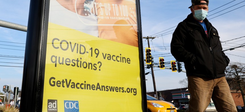 A man walks past a COVID-19 vaccine advertisement poster on the side of a bus stop at the corner of Carleton Avenue and Main Street in East Islip, New York, on December 10, 2021. 