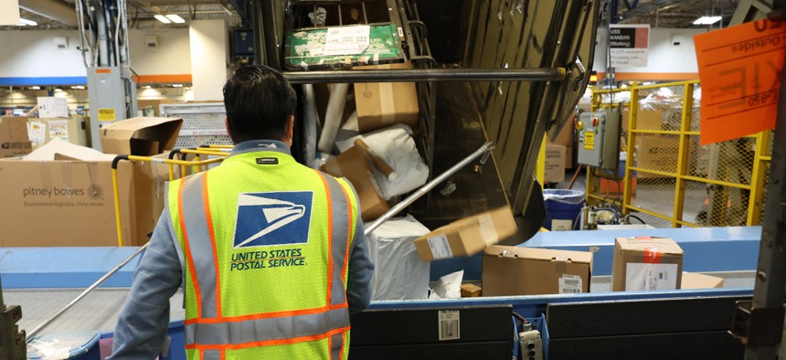 A worker pulls packages from a bin onto a conveyor belt at the U.S. Postal Service Processing And Distribution Center on Dec. 14, 2022 in San Francisco.