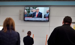 People waiting to meet travelers arriving at the international terminal at O'Hare Airport in Chicago watch as President Donald Trump holds a news conference about the ongoing global coronavirus pandemic on March 13, 2020.