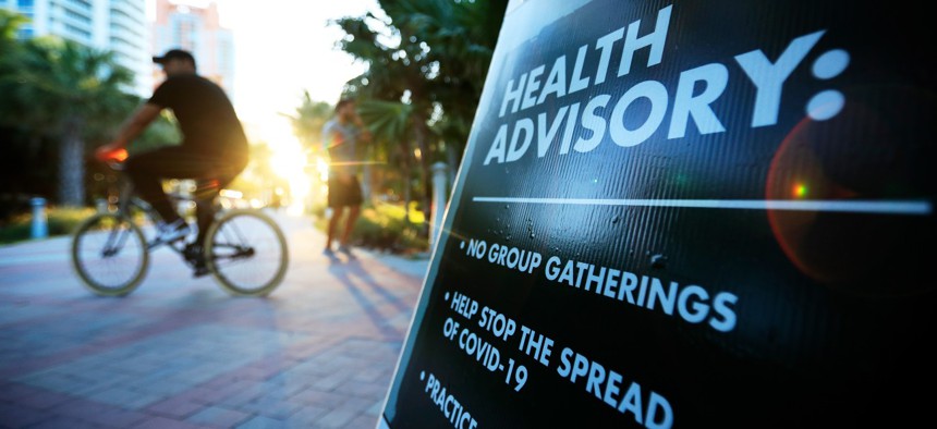 A cyclist passes a “Health Advisory” sign on March 18, 2020, in Miami Beach, Florida, during the early days of the COVID-19 pandemic.