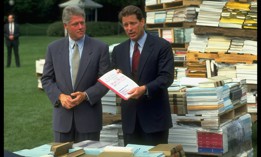 President Bill Clinton looks on as Vice President Al Gore presents his National Performance Review. The two are standing among piles of government regulations.