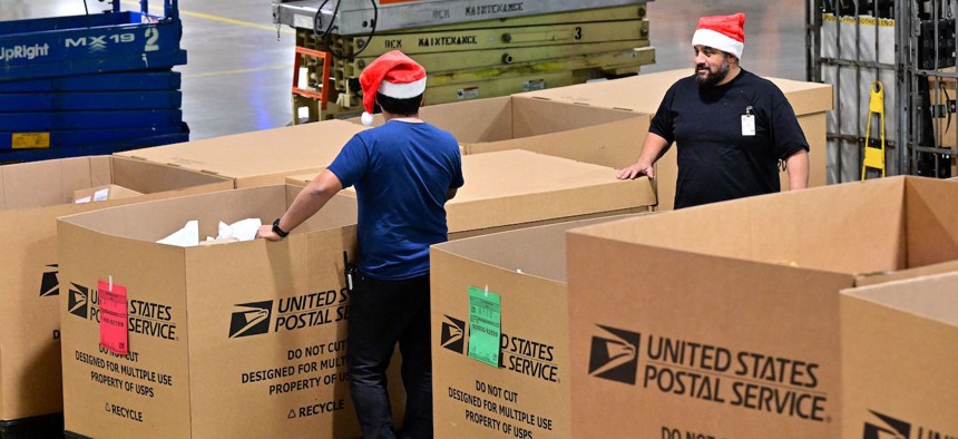 Postal Service employees, some wearing Santa hats, sort mail at the Los Angeles Processing and Distribution Center in preparation for another busy holiday season, Nov. 30, 2022. USPS saw an 11% dip in mail and package volume during its busy holiday season in 2022 compared to the previous year.