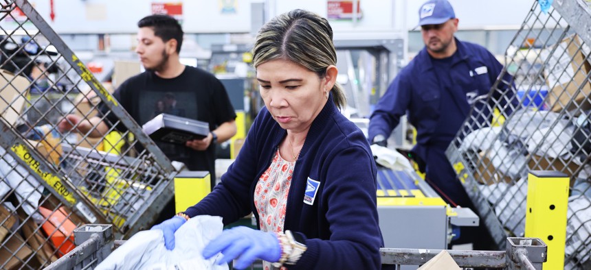 U.S. Postal Service employees place packages into a new package sorting machine, ahead of the holiday mail rush at the Torrance Post Office on Nov. 27, 2023 in Torrance, California.