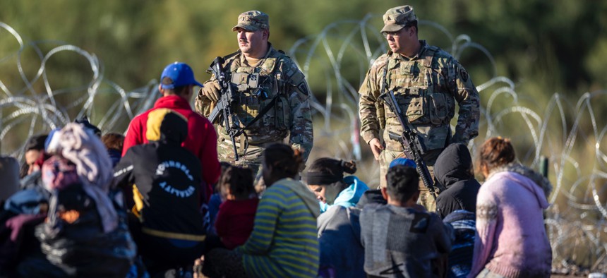 Texas National Guard troops watch over some of more than 1,000 immigrants who had crossed the Rio Grande overnight from Mexico on Dec. 18, 2023 in Eagle Pass, Texas.