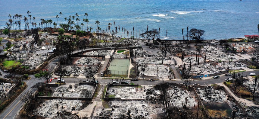 In an aerial view, a recovery vehicle drives past burned structures and cars two months after a devastating wildfire on Oct. 9, 2023 in Lahaina, Hawaii.