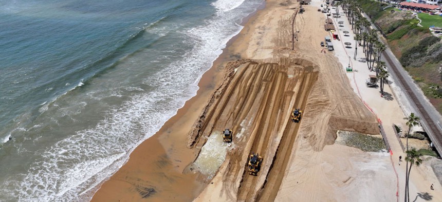 In an aerial view, workers move fresh sand delivered via barge to the main public beach during a sand replenishment project along eroding shoreline on May 21, 2024, in San Clemente, California. 