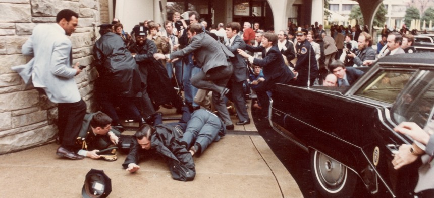 Police officers and Secret Service agents dive to protect President Ronald Reagan amid a panicked crowd during an assassination attempt by John Hinckley Jr. outside the Washington Hilton Hotel, on March 30, 1981. 