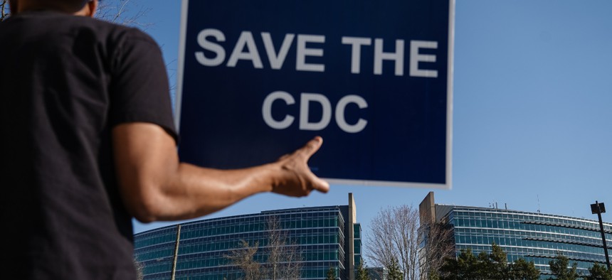 People protesting personnel cuts at the Centers for Disease Control hold signs outside the organization's main headquarters on March 12, 2025 in Atlanta, Georgia.
