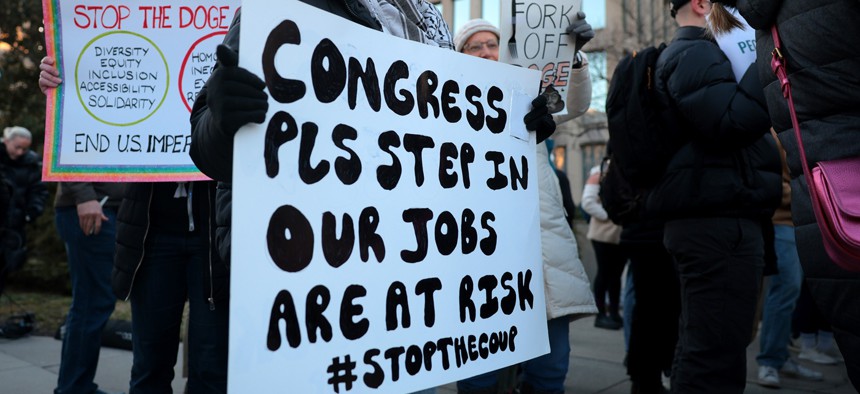 Federal workers and supporters hold signs as they demonstrate against the Department of Government Efficiency outside of the Office of Personnel Management headquarters on February 7, 2025 in Washington, DC.