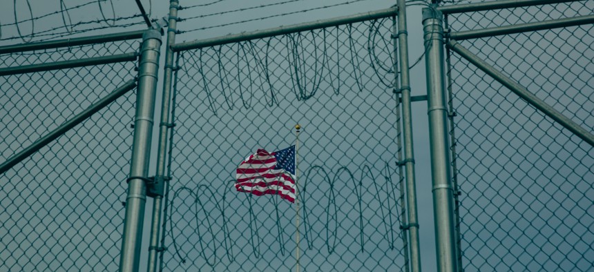 An American flag flies behind barbed wire fencing at the Office of Military Commissions building on June 27, 2023 at Guantanamo Bay, Cuba. The Trump administration has sent about 780 noncitizens to Guantánamo Bay, according to The New York Times.