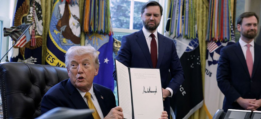 President Donald Trump holds up a document that he signed as Vice President JD Vance, center, and Federal Trade Commission Chairman Andrew Ferguson look on during a White House signing ceremony in the Oval Office of the White House on March 16, 2026 in Washington, DC. Trump signed an executive order to create a task force on fraud which will be lead by Vice President J.D. Vance.