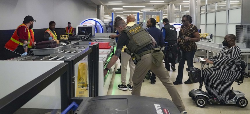 An ICE agent helps load items onto the conveyor belt, with Delta Ramp employees at the TSA security checkpoint at Atlanta Hartsfield-Jackson International Airport on March 27, 2026. The travel disruptions continue as hundreds of TSA agents quit or work without pay during a partial government shutdown. President Donald Trump deployed ICE agents to U.S. airports on Monday, with border czar Tom Homan in charge of the effort. 