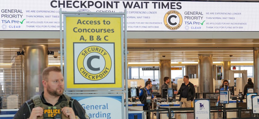 TSA workers assist travelers through security while an ICE agent patrols at BWI Airport on March 30, 2026 in Baltimore. Airports around the country started recovering from long lines as TSA agents begin to receive their first paychecks after working without pay since a partial government shutdown started Feb. 14.