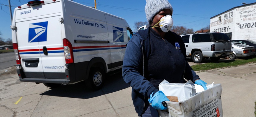 A U.S. Postal worker makes a delivery with gloves and a mask in Warren, Mich., Thursday, April 2.