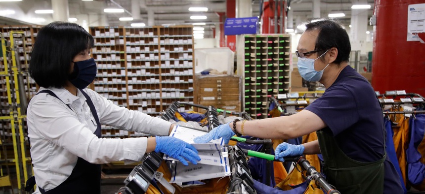 Postal workers May Chen, left, and Wilson Yu wear masks and gloves during the coronavirus pandemic as they sort mail at the United States Postal Service processing and distribution center on April 30 in Oakland, Calif.