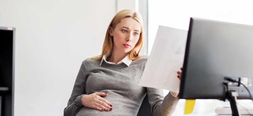A pregnant woman looks at a spreadsheet in an office